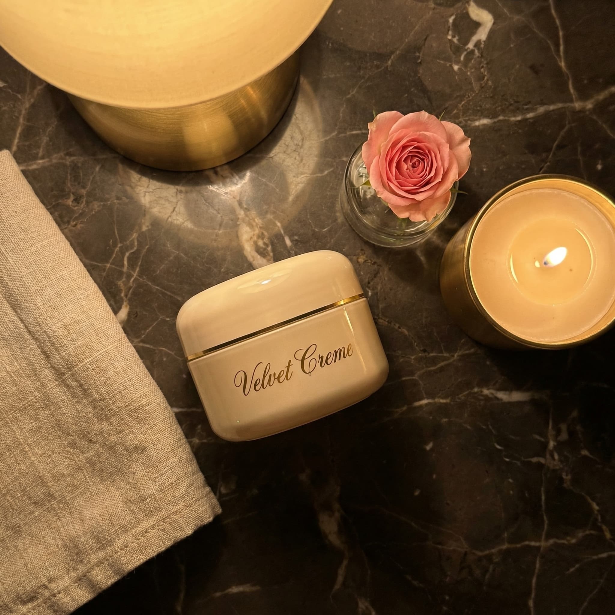 Velvet Creme jar with rose petals and candle on dark surface